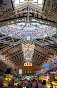 Interior view of the bustling Mercado Central in Valencia, Spain, featuring market stalls and a crowd under the decorative ceiling.