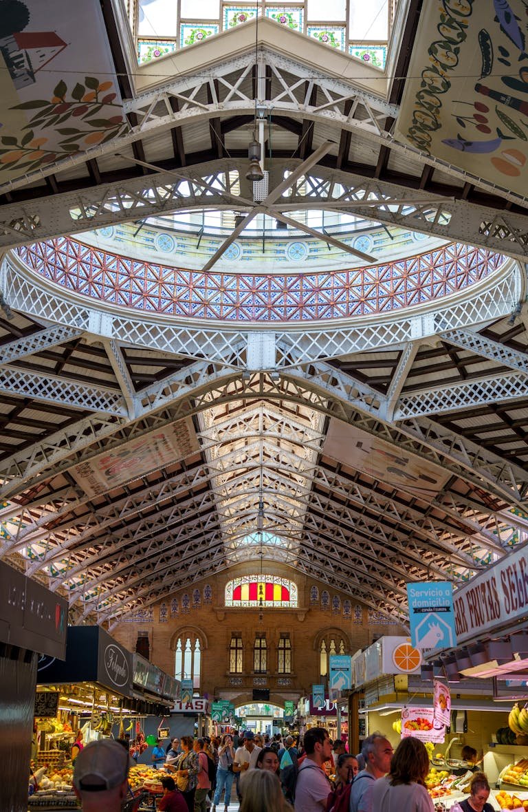 Interior view of the bustling Mercado Central in Valencia, Spain, featuring market stalls and a crowd under the decorative ceiling.